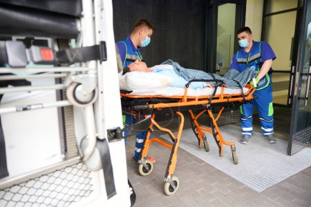 Foto de Los paramédicos hombres entregaron a la víctima en el accidente a la sala de emergencias, el paciente fue fijado en una camilla especial - Imagen libre de derechos