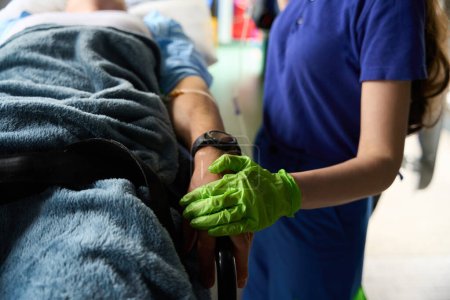 Téléchargez les photos : Une ambulancière fait une goutte d'eau à un patient blessé, elle tient une main d'homme - en image libre de droit