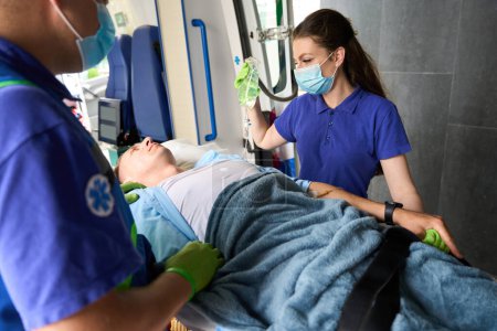 Foto de El paciente, en camilla especial, es trasladado de la ambulancia a la sala de emergencias, al lado de la enfermera está sosteniendo un gotero - Imagen libre de derechos