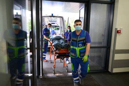 Téléchargez les photos : Une équipe paramédicale a livré une civière avec un patient aux urgences, le personnel médical travaillant dans des masques de protection - en image libre de droit