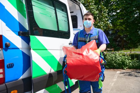 Photo for Medic in uniform carries a special vacuum mattress for transporting patients with polytrauma, next to an ambulance - Royalty Free Image