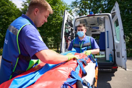 Foto de Médicos arreglan a la víctima en el accidente en una camilla especial, paramédicos en guantes protectores - Imagen libre de derechos