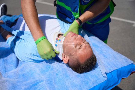 Téléchargez les photos : Employé de l'équipe mobile met un collier sur la victime, le patient s'allonge sur une civière spéciale - en image libre de droit