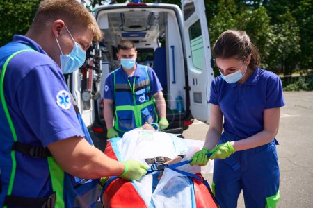 Téléchargez les photos : L'équipe d'ambulance soigne le patient avec des blessures combinées sur un matelas aspirateur, la victime est chargée dans une ambulance - en image libre de droit