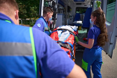 Téléchargez les photos : Les ambulanciers transportent le patient sur une civière spéciale à l'ambulance, les médecins utilisent un matelas aspirateur - en image libre de droit