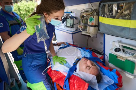 Téléchargez les photos : Le patient est allongé sur une civière dans une ambulance, les ambulanciers expérimentés l'ont mis sous perfusion - en image libre de droit