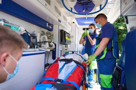 Foto de Médico femenino pone a un paciente en un gotero con medicina, un equipo de paramédicos transporta a un paciente con politraumatismo - Imagen libre de derechos