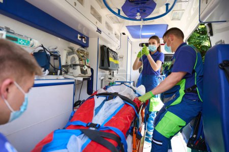Foto de Mujer paramédica pone un gotero con analgésicos en la paciente, un equipo de médicos transporta a un paciente con politraumatismo - Imagen libre de derechos