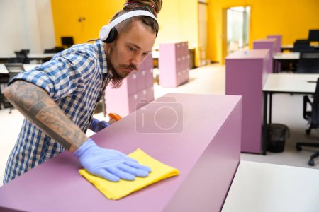 Photo for Guy in headphones rubs a purple locker with a yellow rag, he uses a cleansing spray - Royalty Free Image