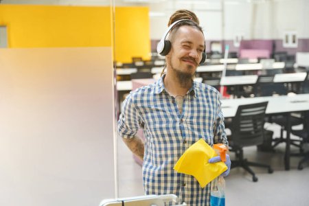 Photo for Tired cleaner in protective gloves holds on to his back, he listens to music in headphones - Royalty Free Image