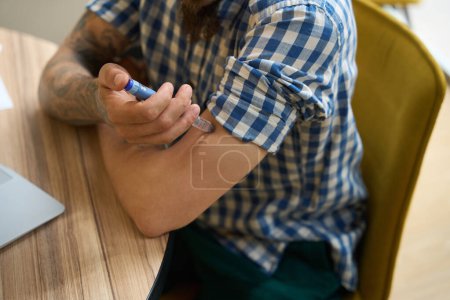 Foto de El hombre con una camisa a cuadros se inyecta en el brazo, se sienta en su escritorio - Imagen libre de derechos