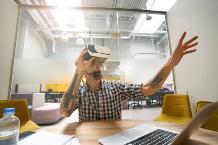 Foto de Informal freelancer utiliza un auricular de realidad virtual, se sienta en su escritorio en un espacio de coworking - Imagen libre de derechos