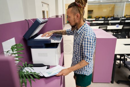 Photo for Freelancer in a plaid shirt uses a photocopier in a coworking space, he copies work documents - Royalty Free Image