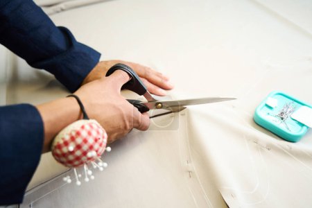 Photo for Closeup of dressmaker hands scissoring out fabric pattern pieces in sewing workshop - Royalty Free Image