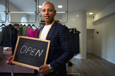 Photo for Joyous clothier holding black signboard with word Open written in white chalk in atelier - Royalty Free Image