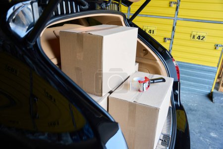 Foto de Coche con un baúl abierto en un almacén, hay un montón de cajas de cartón en el baúl - Imagen libre de derechos