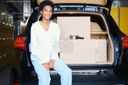 Foto de Joven cliente trajo cajas de cartón en el almacenamiento, la mujer se sentó en el borde del maletero - Imagen libre de derechos