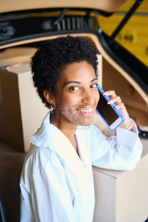 Photo for Woman in casual clothes communicates on the phone in a storage room near her car - Royalty Free Image