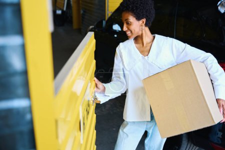 Téléchargez les photos : Femme afro-américaine chargeant une boîte en carton dans un casier à côté de sa voiture - en image libre de droit