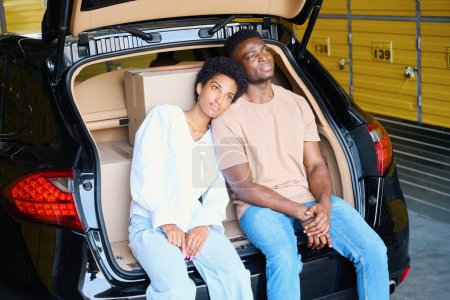 Téléchargez les photos : Les Afro-Américains sont assis blottis ensemble dans un coffre ouvert, boîtes avec des choses dans la voiture - en image libre de droit
