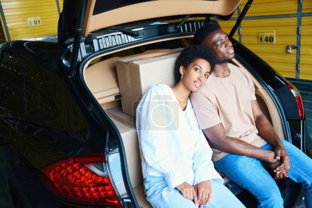 Photo for Young guys are sitting huddled together in an open trunk, boxes with things in the car - Royalty Free Image