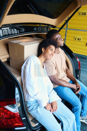 Téléchargez les photos : Guy et sa copine sont assis blottis ensemble dans le coffre, il y a des boîtes avec des choses dans la voiture - en image libre de droit