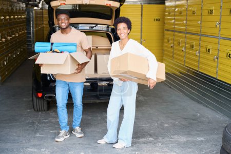 Photo for Young woman and her friend unload boxes with things from the trunk, yellow storage cells indoors - Royalty Free Image
