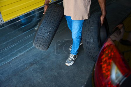 Téléchargez les photos : Le type en jeans a apporté des pneus de voiture pour le stockage saisonnier, il utilise un service de stockage - en image libre de droit