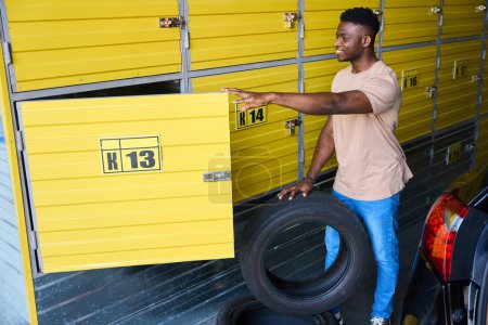 Téléchargez les photos : Pilote charge des pneus de voiture dans un casier pour le stockage saisonnier, il utilise un service de stockage - en image libre de droit