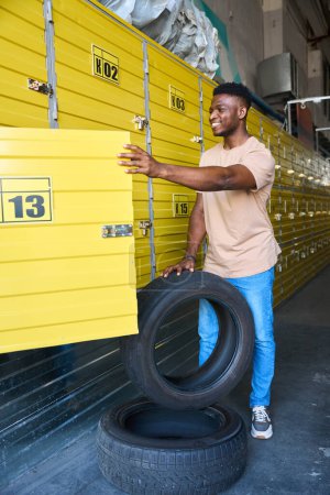 Téléchargez les photos : Un gars charge des pneus de voiture dans un casier pour le stockage saisonnier, il utilise un service de stockage - en image libre de droit