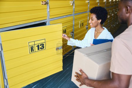 Foto de Mujer gerente abre una caja de almacenamiento para un cliente, y un hombre tiene una caja de cartón - Imagen libre de derechos