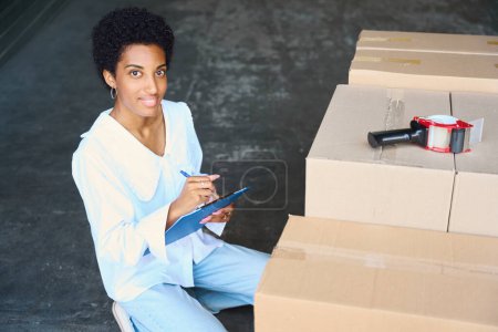 Téléchargez les photos : Femme fait un inventaire des choses déposées, il y a beaucoup de boîtes en carton devant elle - en image libre de droit