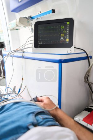 Foto de El hombre con ropa casual está conectado a un cardiógrafo en una ambulancia, los indicadores de los pacientes se muestran en el monitor - Imagen libre de derechos