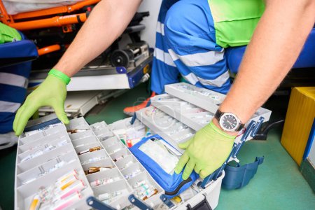 Photo for Paramedic opened suitcase with set of medicines to provide emergency care to a patient, the medic works in protective gloves - Royalty Free Image