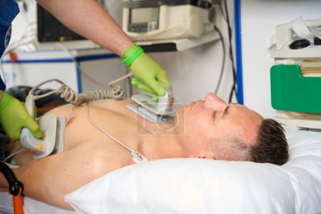 Photo for Paramedic applies defibrillator electrodes to a patient torso as he performs CPR on a patient in an ambulance - Royalty Free Image