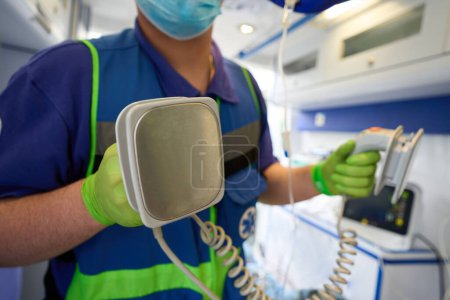 Téléchargez les photos : Médecin ambulancier avec électrodes de défibrillateur dans ses mains, un ambulancier est dans une ambulance - en image libre de droit