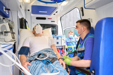 Photo for Paramedic is near a patient in an ambulance, the patient is wearing an oxygen mask - Royalty Free Image