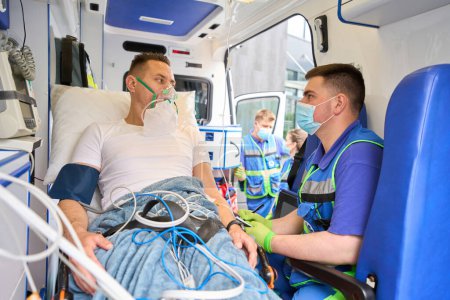 Téléchargez les photos : Les ambulanciers enregistrent les réponses des patients en ambulance, la victime portant un masque à oxygène - en image libre de droit