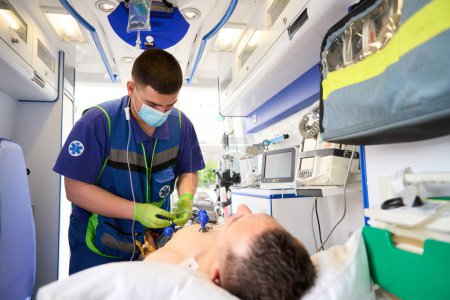Foto de El médico fija electrodos en ventosas al torso de un hombre en una ambulancia para tomar un cardiograma - Imagen libre de derechos