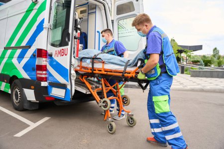Foto de Colegas de paramédicos descargan una camilla con un paciente de una ambulancia, en el coche hay equipos modernos - Imagen libre de derechos