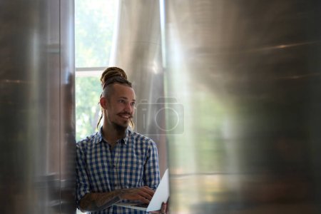 Foto de El hombre joven se para con el portátil a las columnas decorativas en la habitación con el interior moderno - Imagen libre de derechos