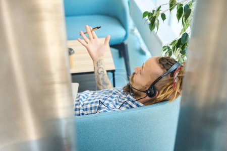 Photo for Freelancer uses a modern laptop and headset in his work, the guy sits on a sofa in a coworking space - Royalty Free Image