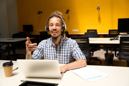 Foto de Hombre informal en una camisa a cuadros se comunica en línea en un escritorio de la oficina, un chico utiliza un auricular para el trabajo - Imagen libre de derechos