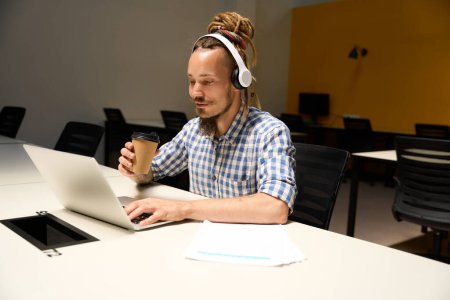 Photo for Guy with dreadlocks communicates online at an office desk, he uses a headset for work - Royalty Free Image