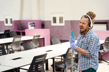 Téléchargez les photos : Le type en casque chante pendant le nettoyage du bureau, un intérieur élégant dans un espace de coworking - en image libre de droit