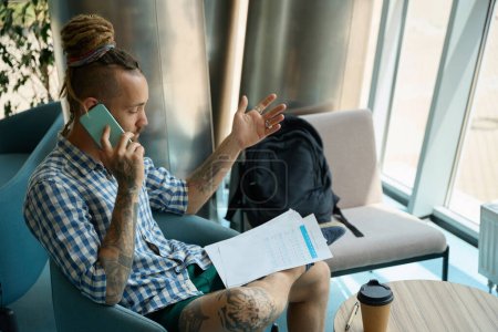 Foto de Hombre estudia los documentos de trabajo y se comunica por teléfono, él está sentado en una silla junto a la mirilla - Imagen libre de derechos