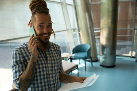 Photo for Smiling freelancer with dreadlocks is on the phone, he is in a comfortable coworking area - Royalty Free Image