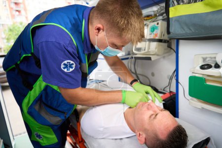 Téléchargez les photos : Homme ambulancier met un goutte à goutte sur un patient dans une ambulance, dans la voiture il y a de l'équipement moderne - en image libre de droit