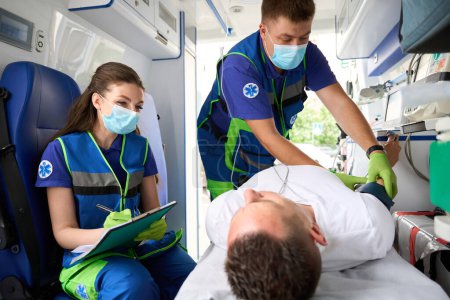 Foto de El equipo de ayuda pronto examina al paciente en la ambulancia, la doctora realiza una encuesta - Imagen libre de derechos