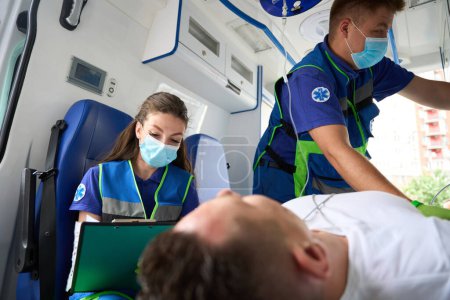 Photo for Paramedics transport a patient in an ambulance, a nurse fills out a patient questionnaire - Royalty Free Image